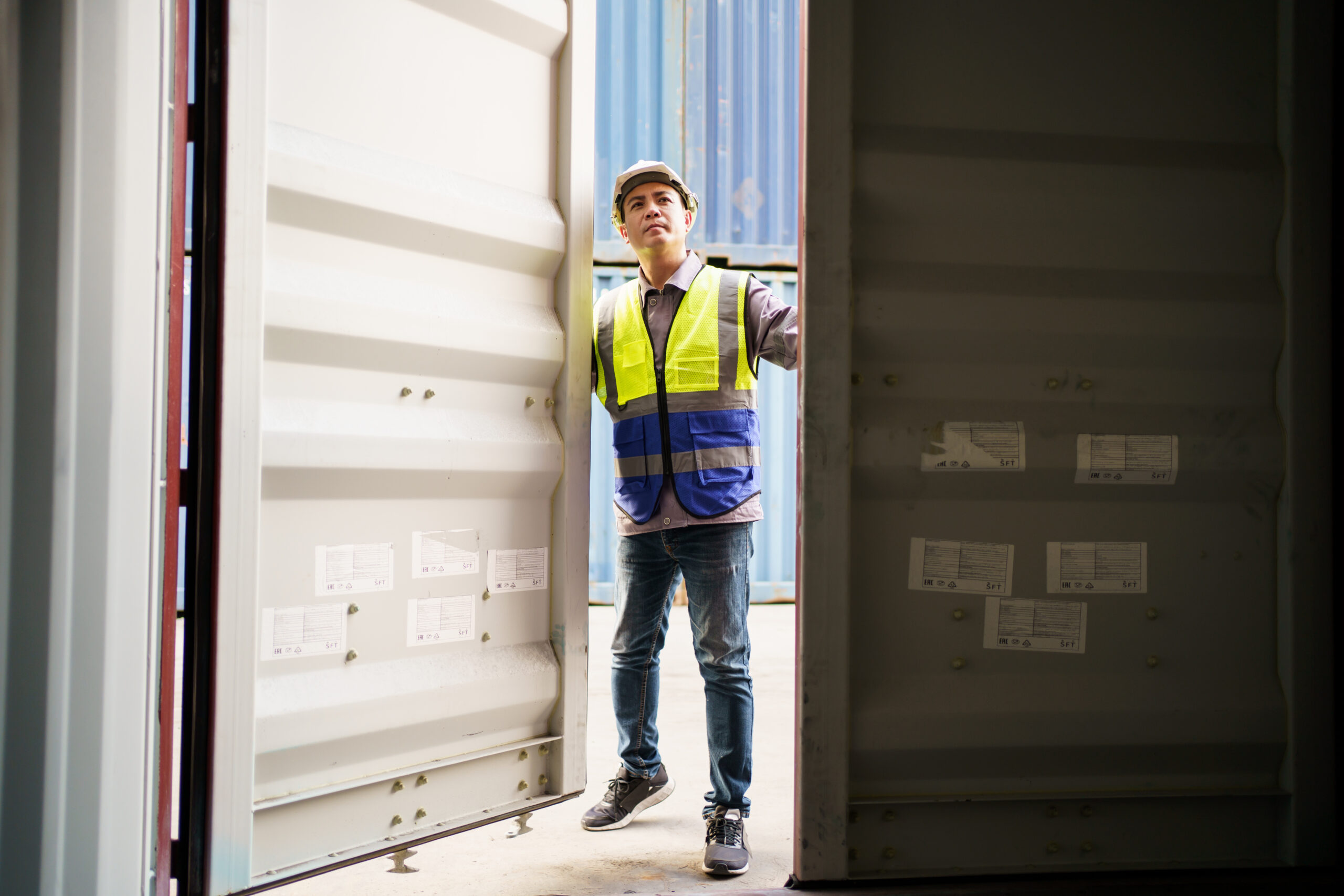 Asian male shipyard engineer is inspecting import or export cargo containers at the container yard. A customs clearance officer inspects against the import - export cargo.